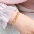 Close-up of a hand wearing gold jewelry with a soft pink background