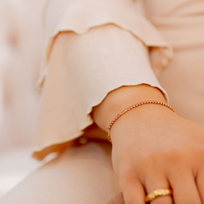 Close-up of a hand wearing a gold bracelet and ring on a blurred  Harma jewelry gold plated I Am Becoming PINK Link Bracelet background