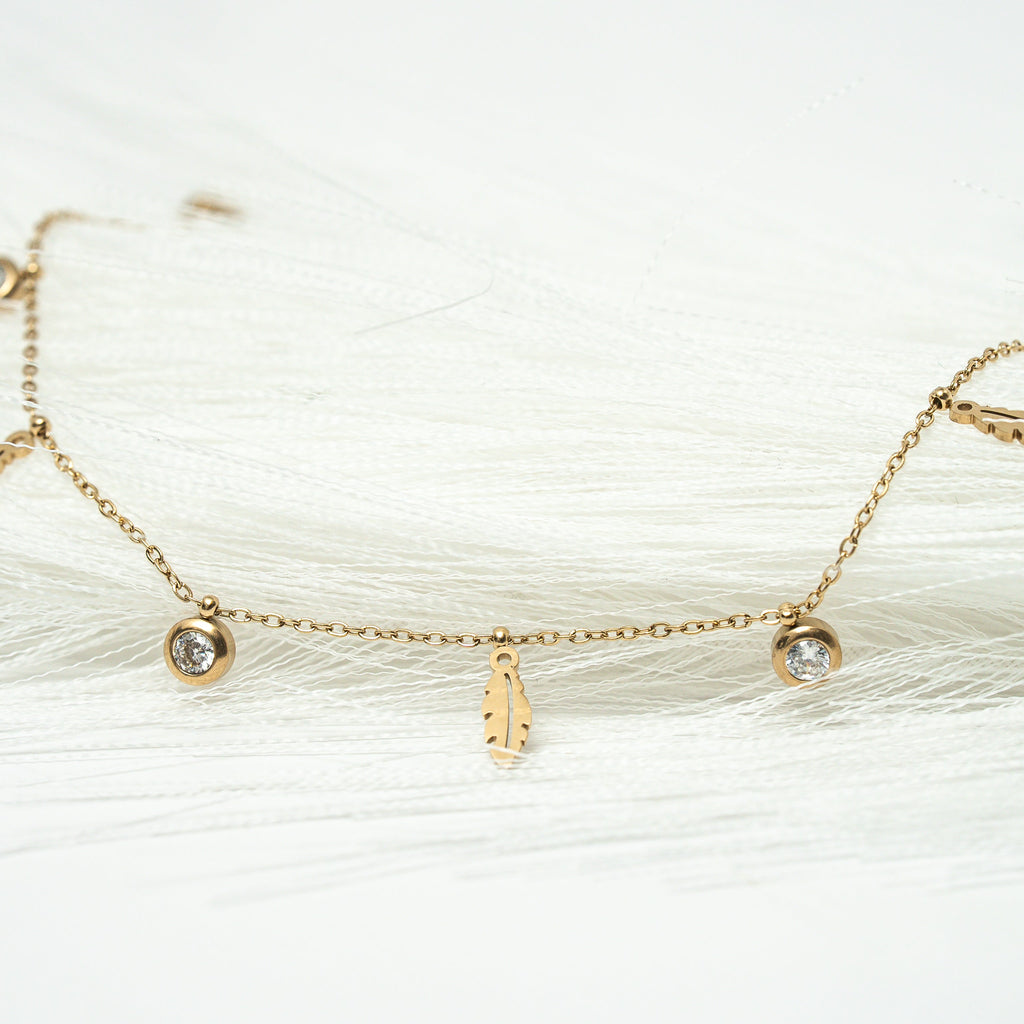 Gold bracelet with small charms on a white background. Harma jewelry gold plated I Am Light Feather Bracelet