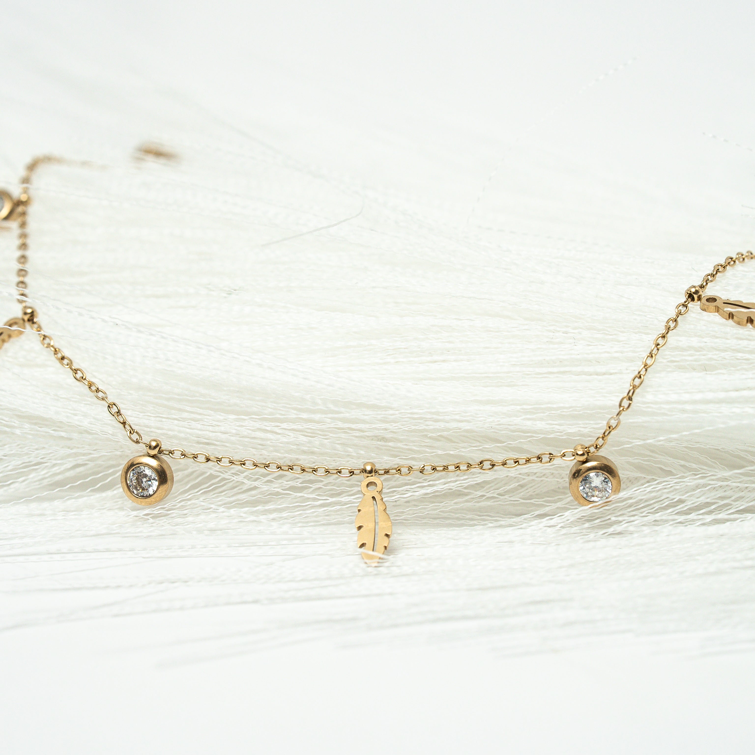 Gold bracelet with small charms on a white background. Harma jewelry gold plated I Am Light Feather Bracelet