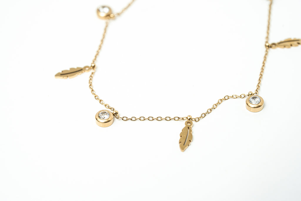 Gold anklet with feather and round charm on a white background. Harma jewelry gold plated I Am Light Feather Bracelet
