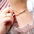 Close-up of a child's hand wearing a gold ring and bracelet on a pink fabric background. Harma jewelry gold plated I Am Loved Crystal Heart Bracelet