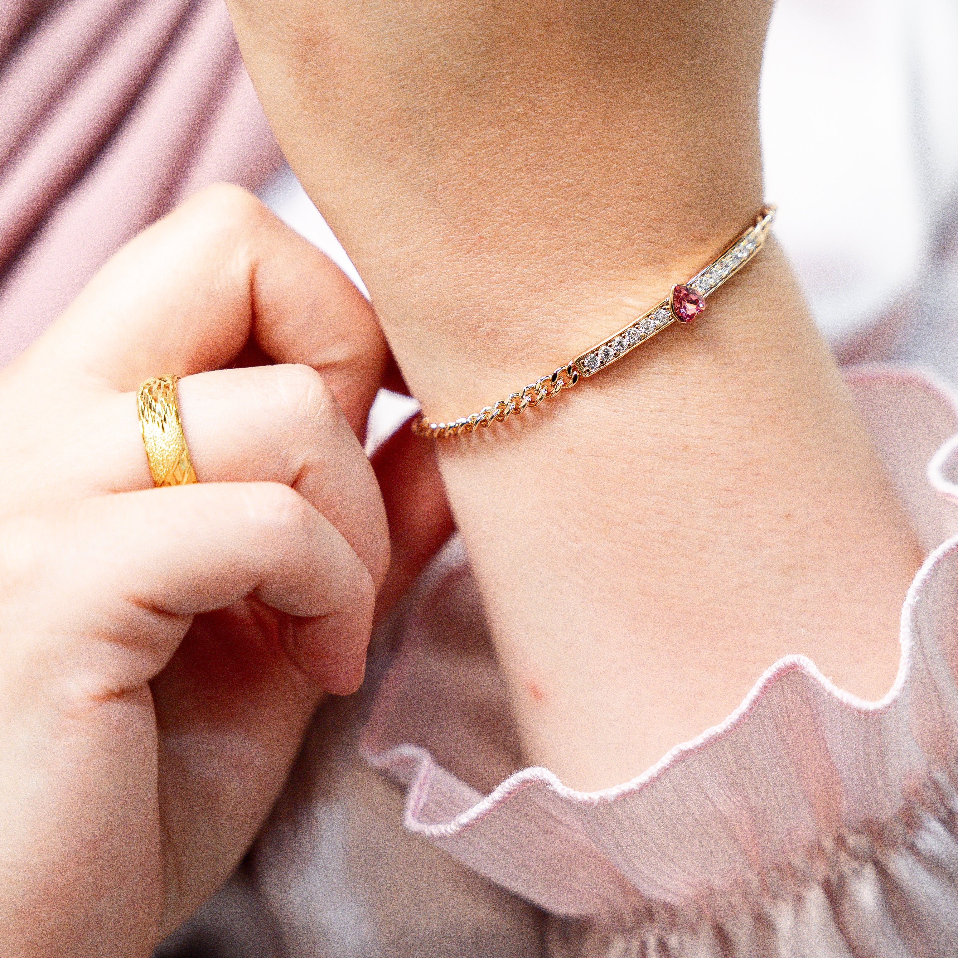 Close-up of a child's hand wearing a gold ring and bracelet on a pink fabric background. Harma jewelry gold plated I Am Loved Crystal Heart Bracelet