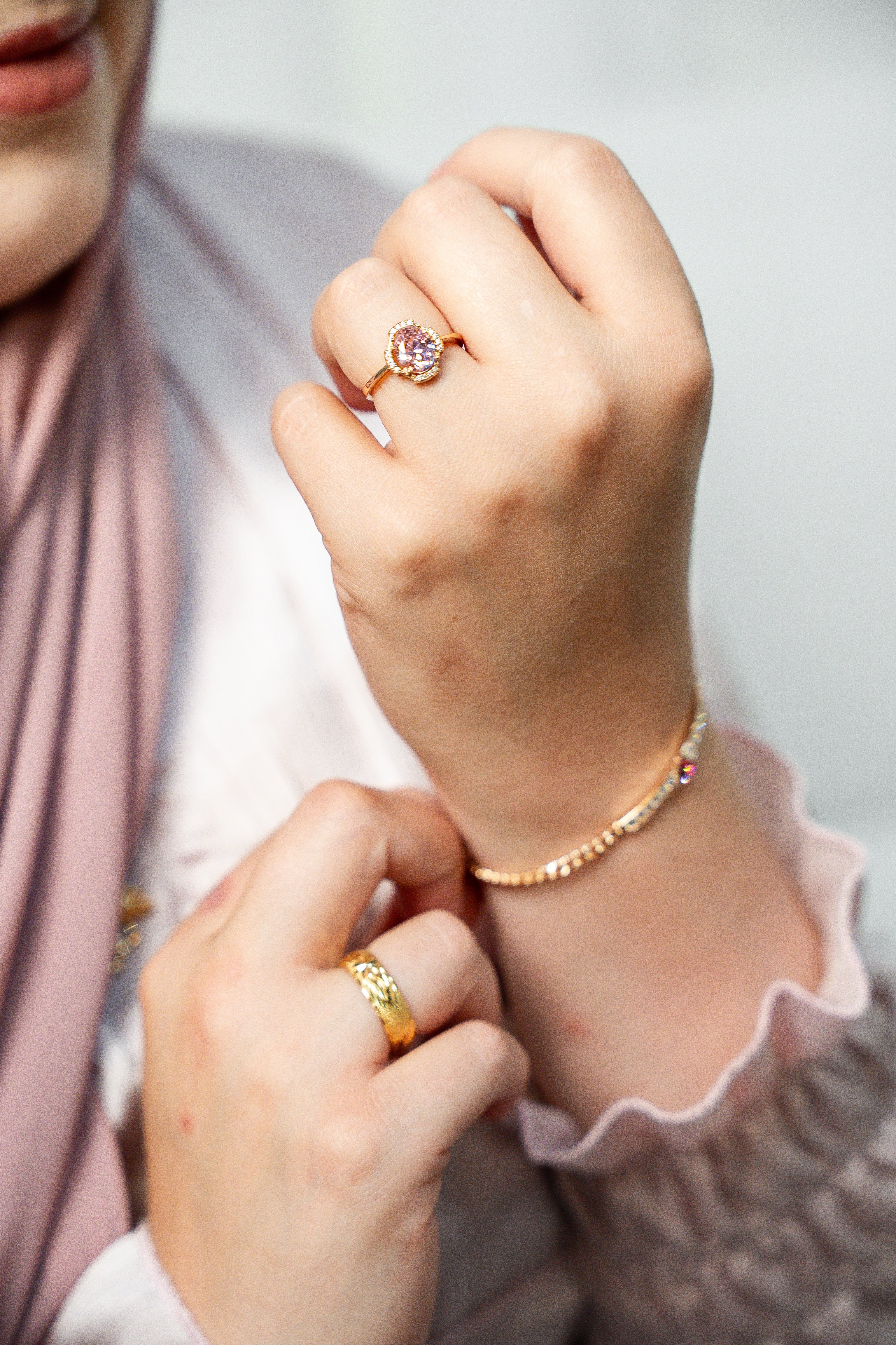 Close-up of a hand wearing a gold ring with a pink gemstone, with a blurred background. Harma jewelry gold plated I Am Loved Crystal Heart Bracelet