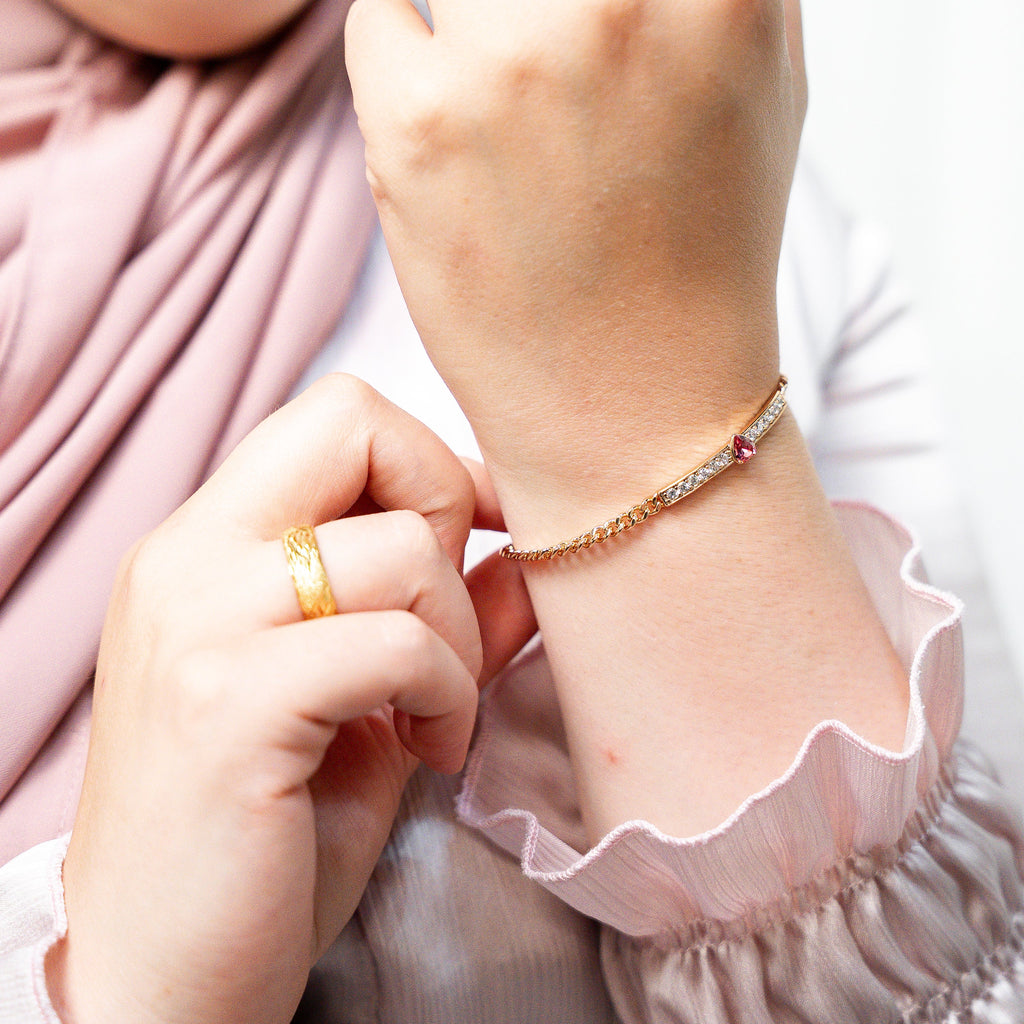 Person wearing a bracelet and ring with a blurred background. Harma jewelry gold plated I Am Loved Crystal Heart Bracelet