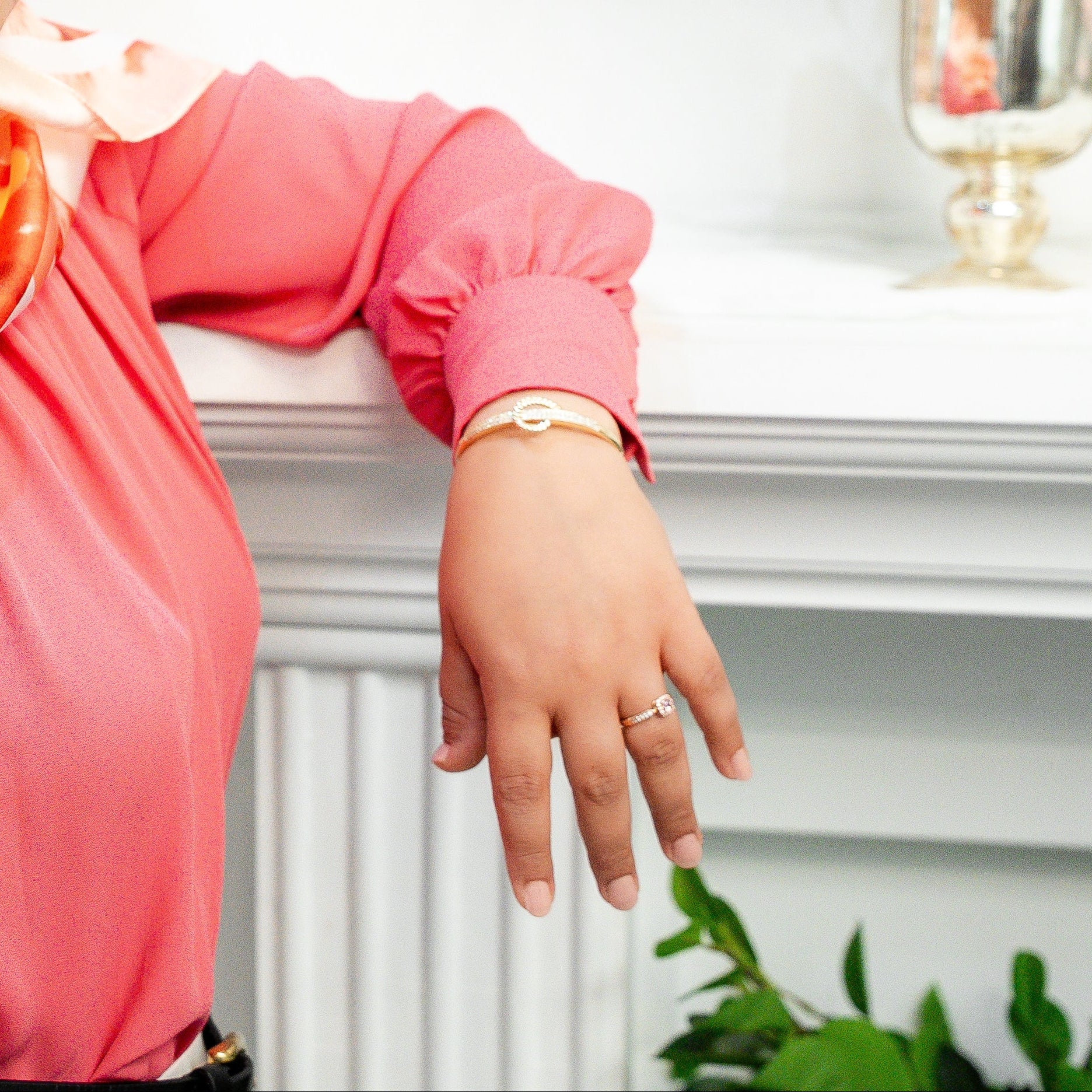 Woman wearing a colorful hijab and pink top leaning against a white wall with flowers in the background Harma jewelry gold plated I Am at Peace Vine Hoop Bangle Bracelet