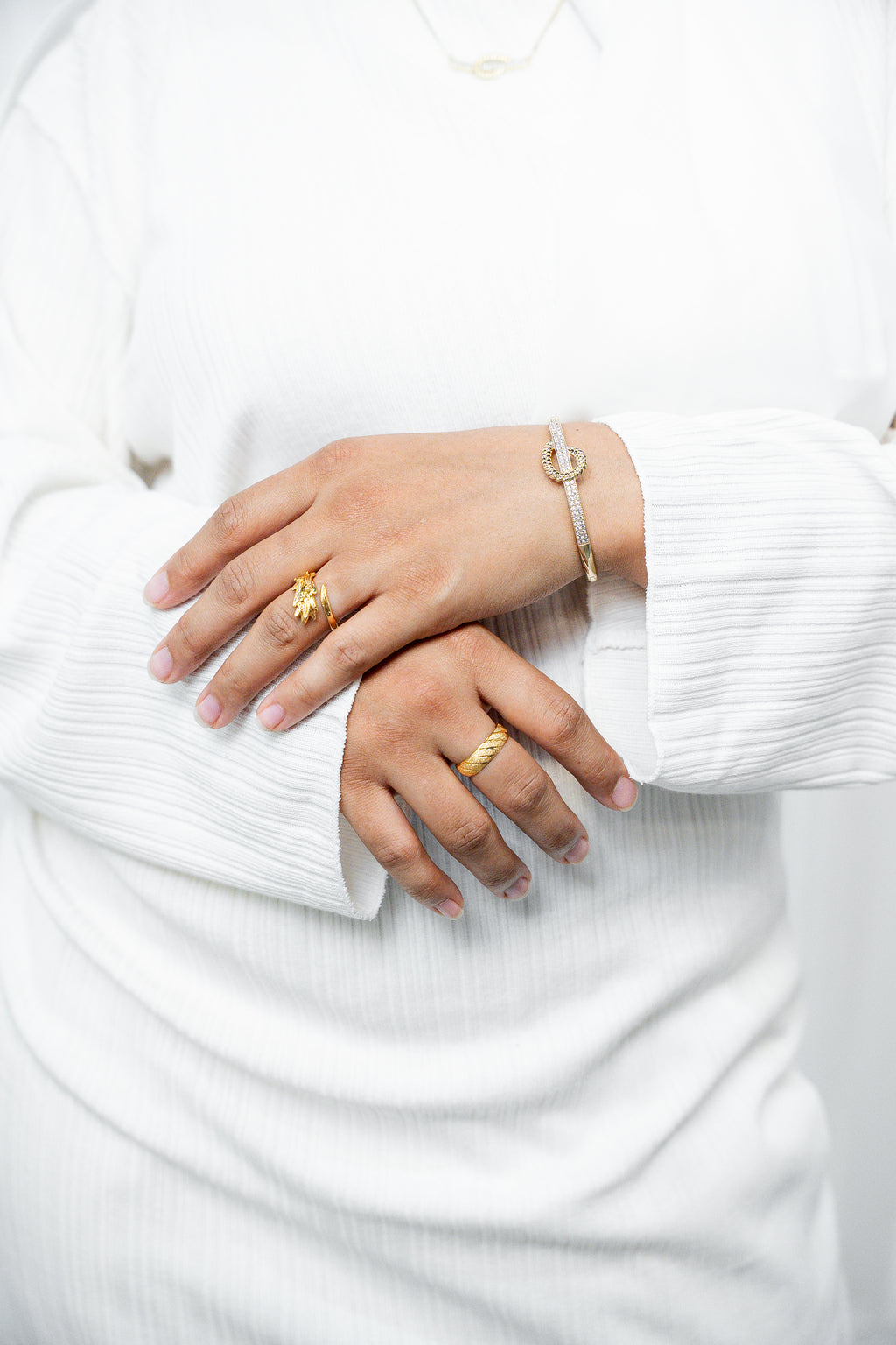 Close-up of hands wearing gold rings and a bracelet on a white background. Harma jewelry gold plated I Am at Peace Vine Hoop Bangle Bracelet