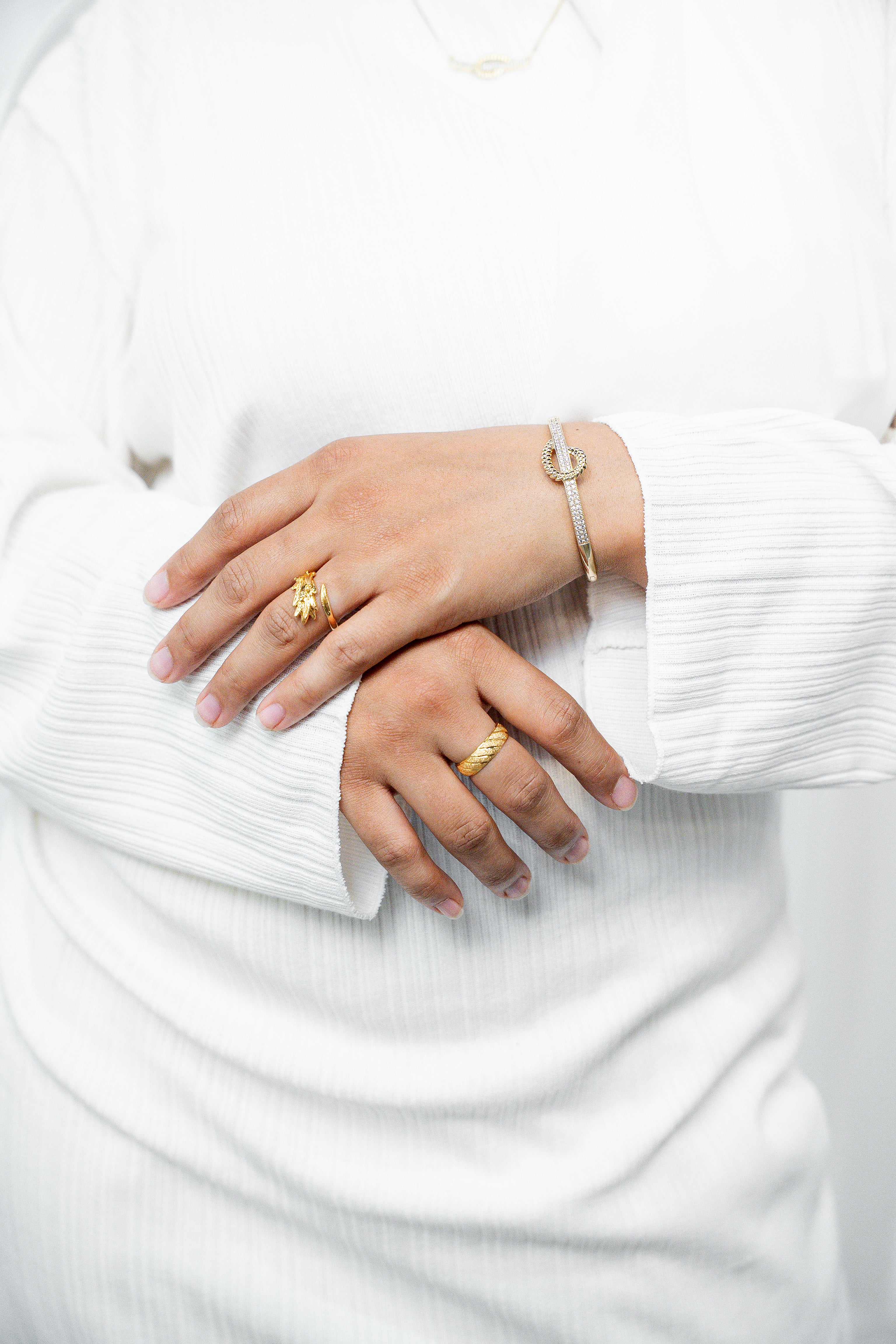 Close-up of hands wearing gold rings and a bracelet on a white background. Harma jewelry gold plated I Am at Peace Vine Hoop Bangle Bracelet