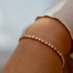 Close-up of a person's arm wearing a delicate bracelet with pink stones on a blurred background. Harma jewelry gold plated Moments of PINK Tennis Bracelet