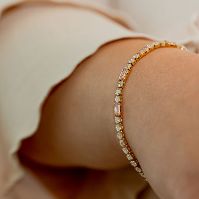 Gold bracelet on a wrist with a blurred background.Harma jewelry gold plated Moments of PINK Tennis Bracelet