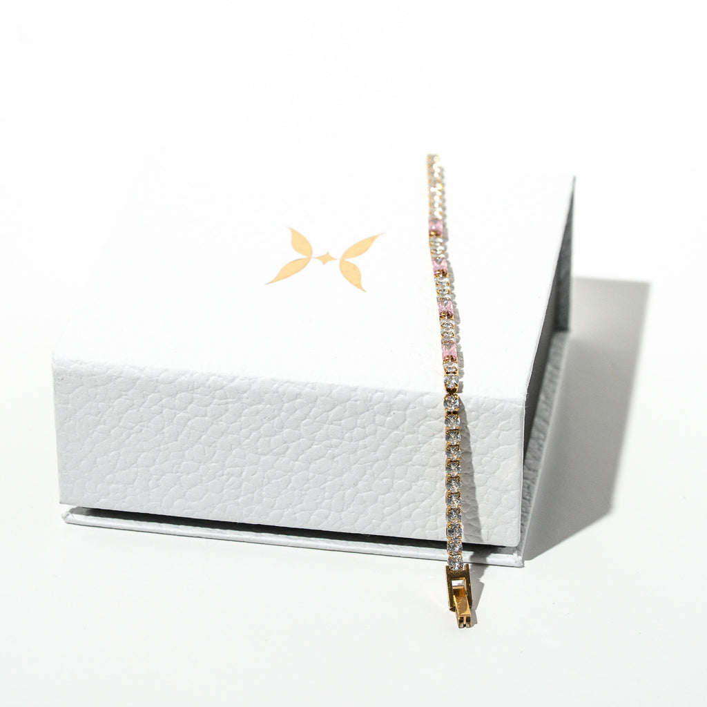 Bracelet displayed on a white box with a brand logo in the corner. Harma jewelry gold plated Moments of PINK Tennis Bracelet