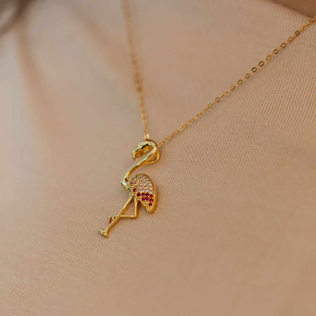 Gold flamingo pendant necklace on a person wearing a sheer top. Harma jewelry s925 I Am Becoming PINK Again Flamingo Necklace 1