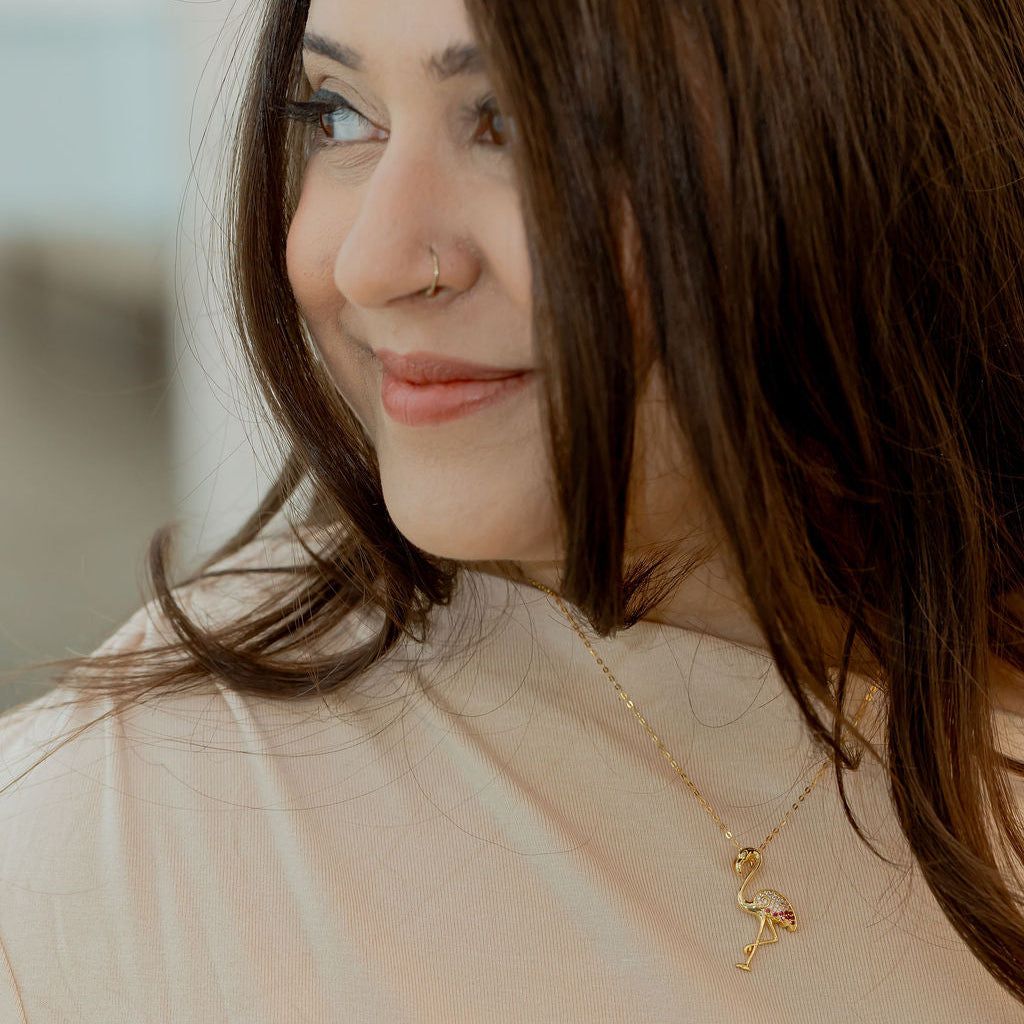 Woman wearing a gold necklace with a pendant, looking to the side. Harma jewelry s925 I Am Becoming PINK Again Flamingo Necklace 1