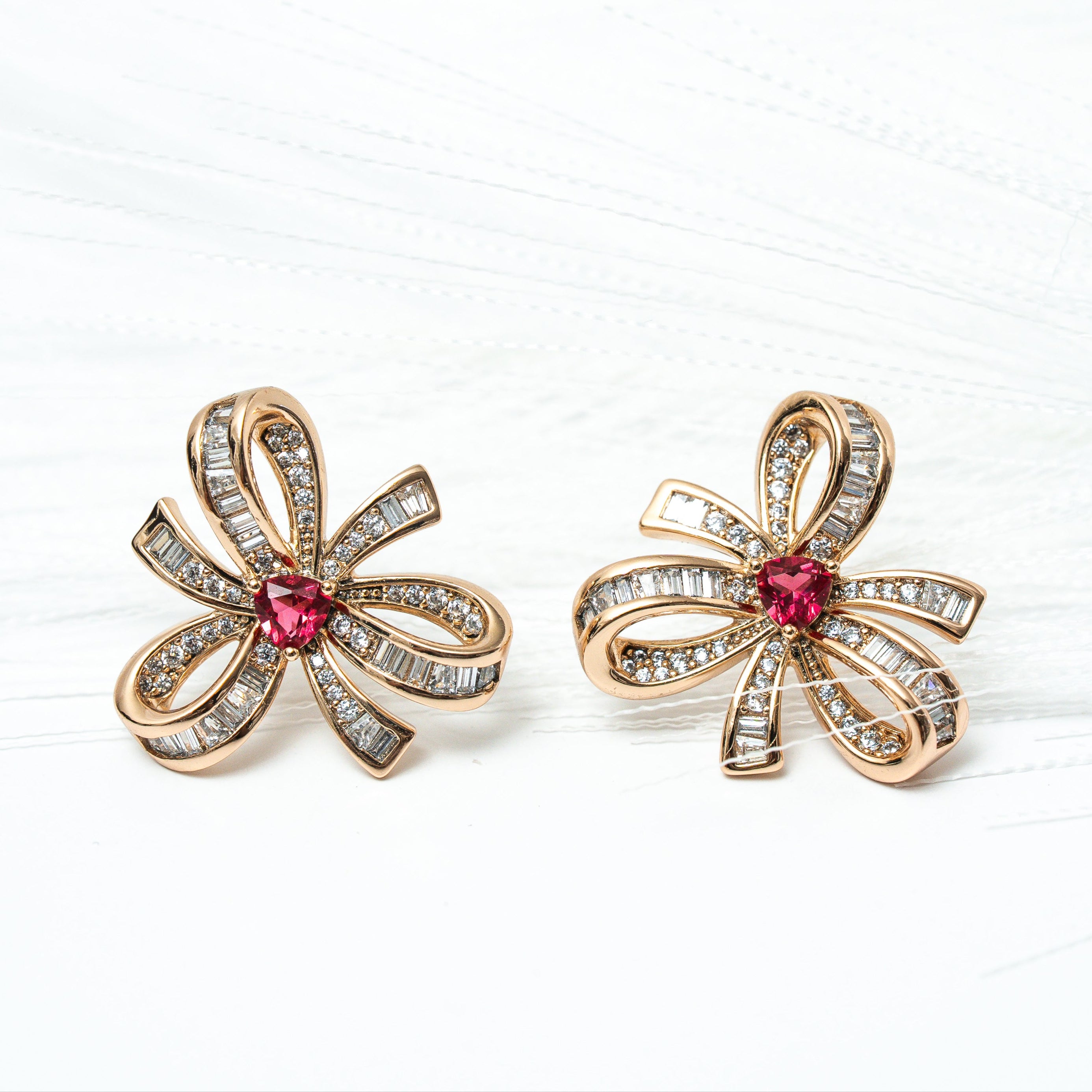 Pair of gold flower-shaped earrings with red gemstones on a white background. Harma gold plated I Am Radiant Bow Stud Earrings