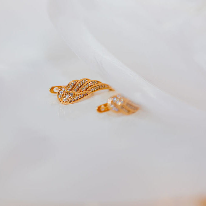 Gold ring with leaf design on a white fabric background. Harm Rise Again Crystal Wings Earrings