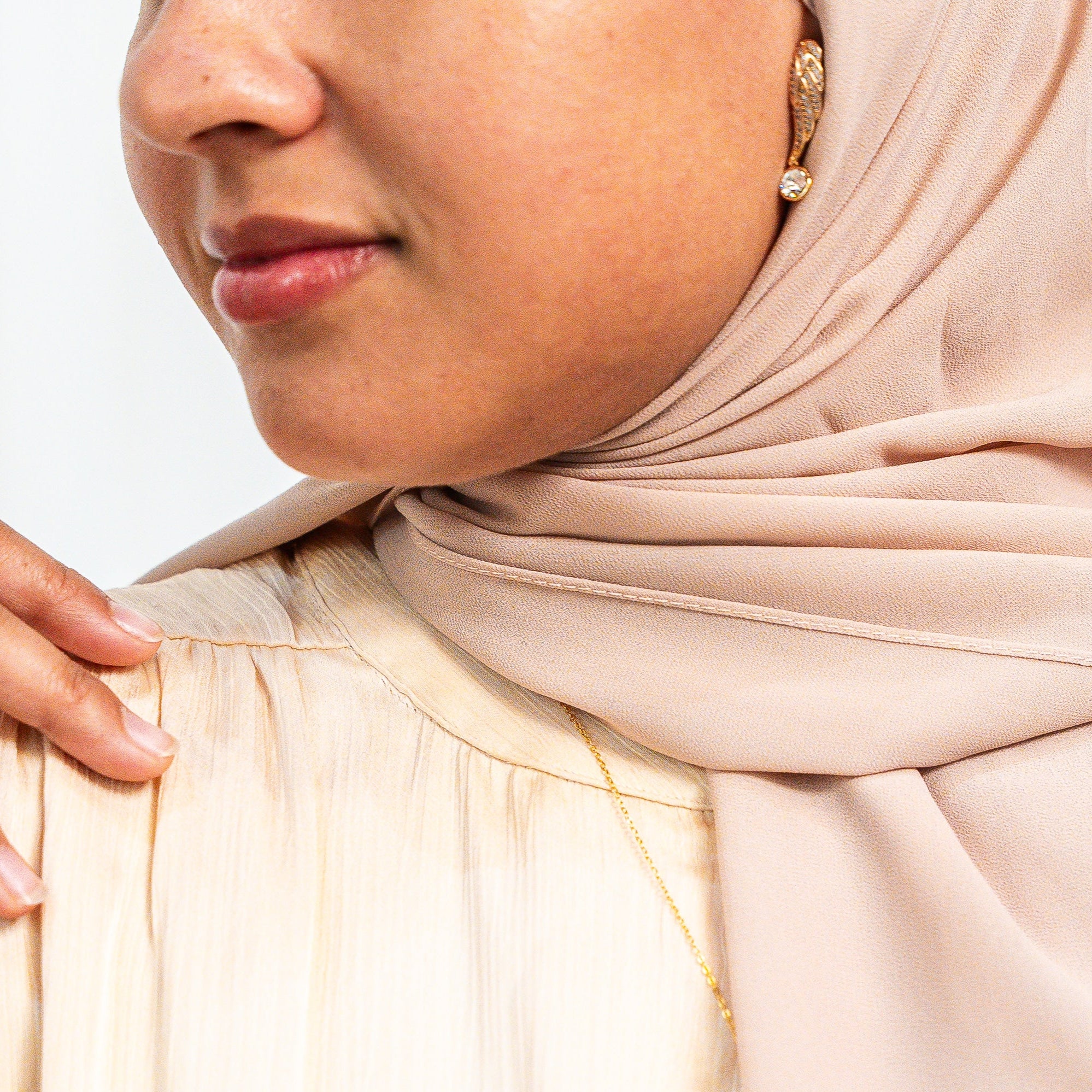 Woman wearing a beige hijab and beige top with a blurred background. Harma Rise Again Crystal Wings Earrings