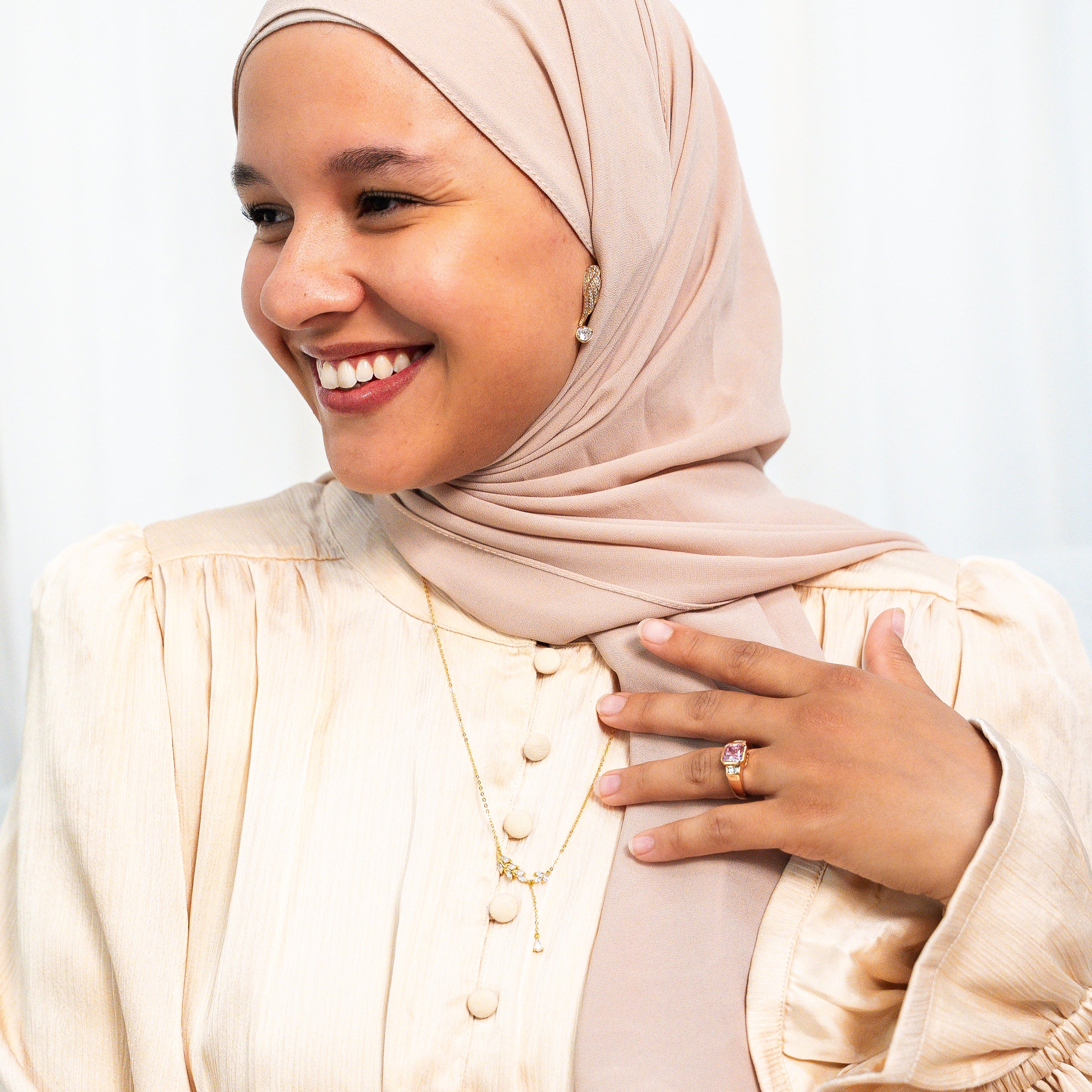 Woman wearing a beige hijab and dress against a white background. Harma Rise Again Crystal Wings Earrings