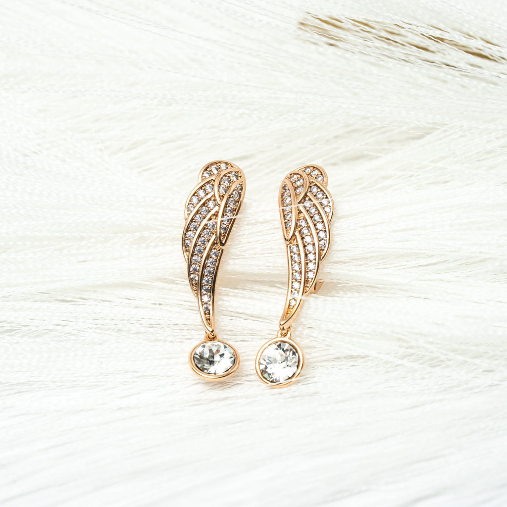 Rose gold angel wing earrings with clear gemstones on a light background