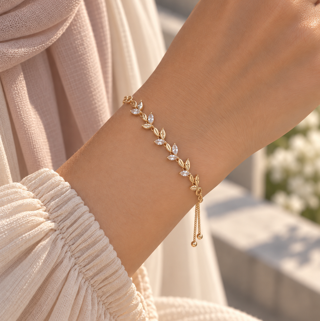 A delicate gold leaf bracelet with clear crystal accents worn on a person's wrist, paired with a cream-colored pleated top and a soft beige scarf. Whispering Magnolia Marquise Adjustable Bracelet 18k gold plated Harma Jewelry