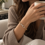 A close-up lifestyle shot of a woman wearing a gold chain-link bracelet with pavé-set clear stones on her wrist, holding a ceramic mug while wearing a brown knit cardigan. Élan Pavé Link Zirconia Bracelet 18k gold plated harma jewelry