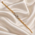 A gold chain bracelet with a central interlocking double-O charm paved with clear stones, displayed on a draped cream satin fabric background. lan_Pave_Link_Zirconia_Bracelet_18k_gold_plated_harma_jewelry_1